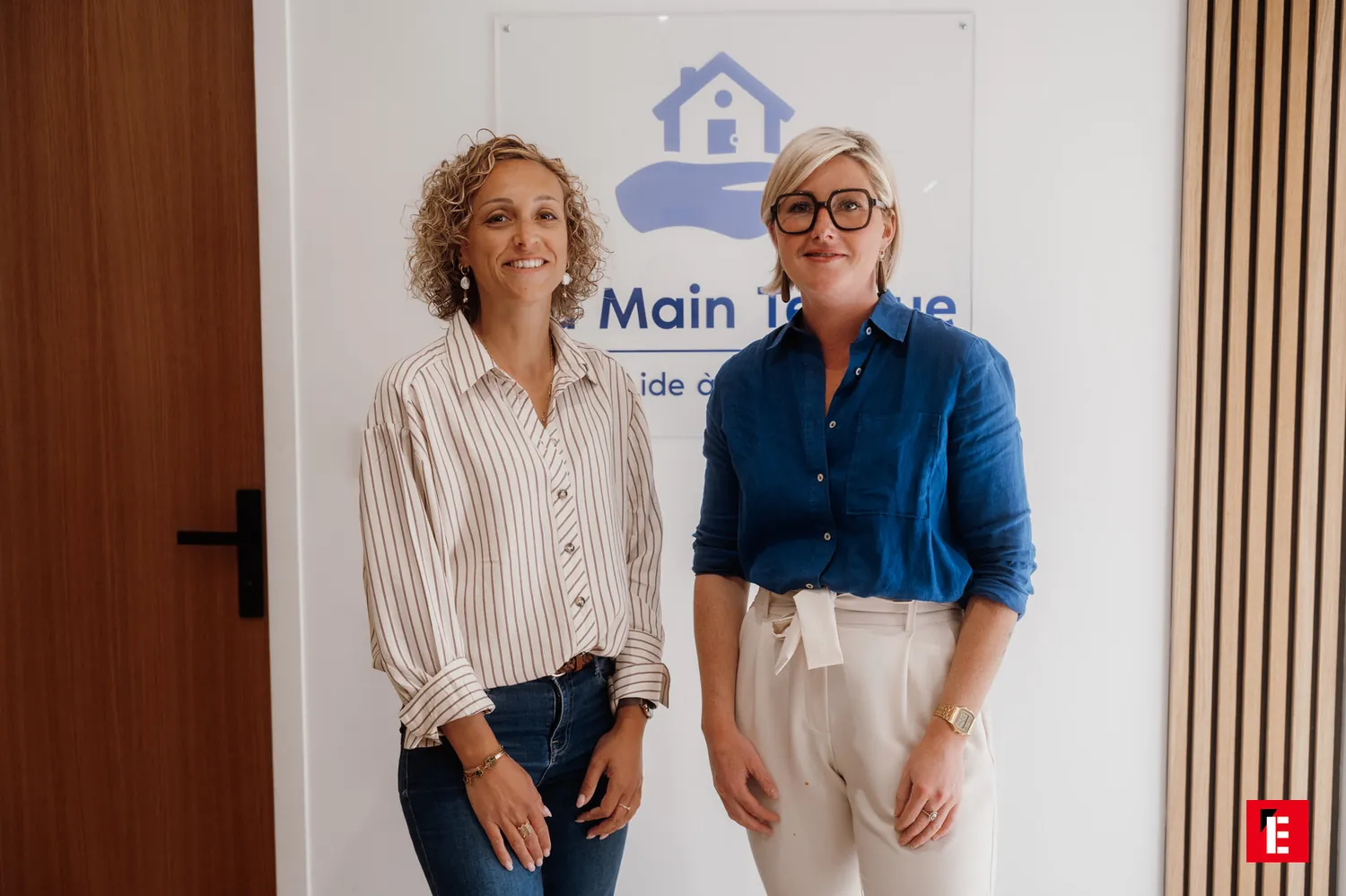 Angélique Béret et Louise Nio, debout devant le panneau La Main Tendue de leur agence de Muzillac.